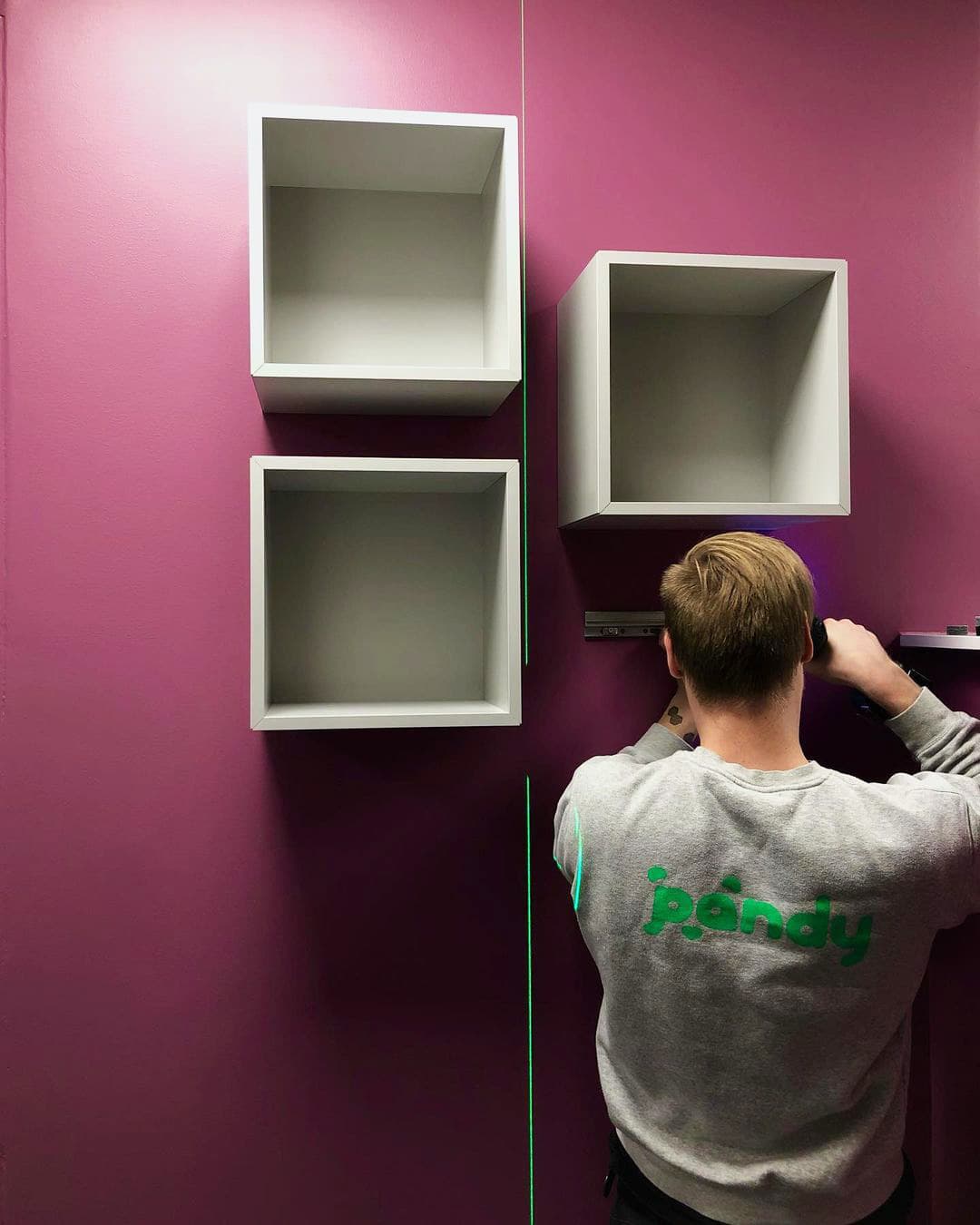 Pandy handyman mounting shelves on a colourful wall