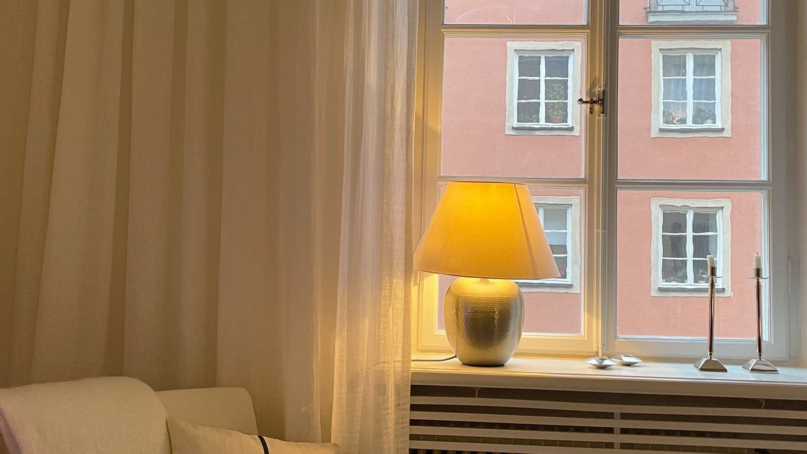 White curtain next to a large window, with a lit lamp on the windowsill