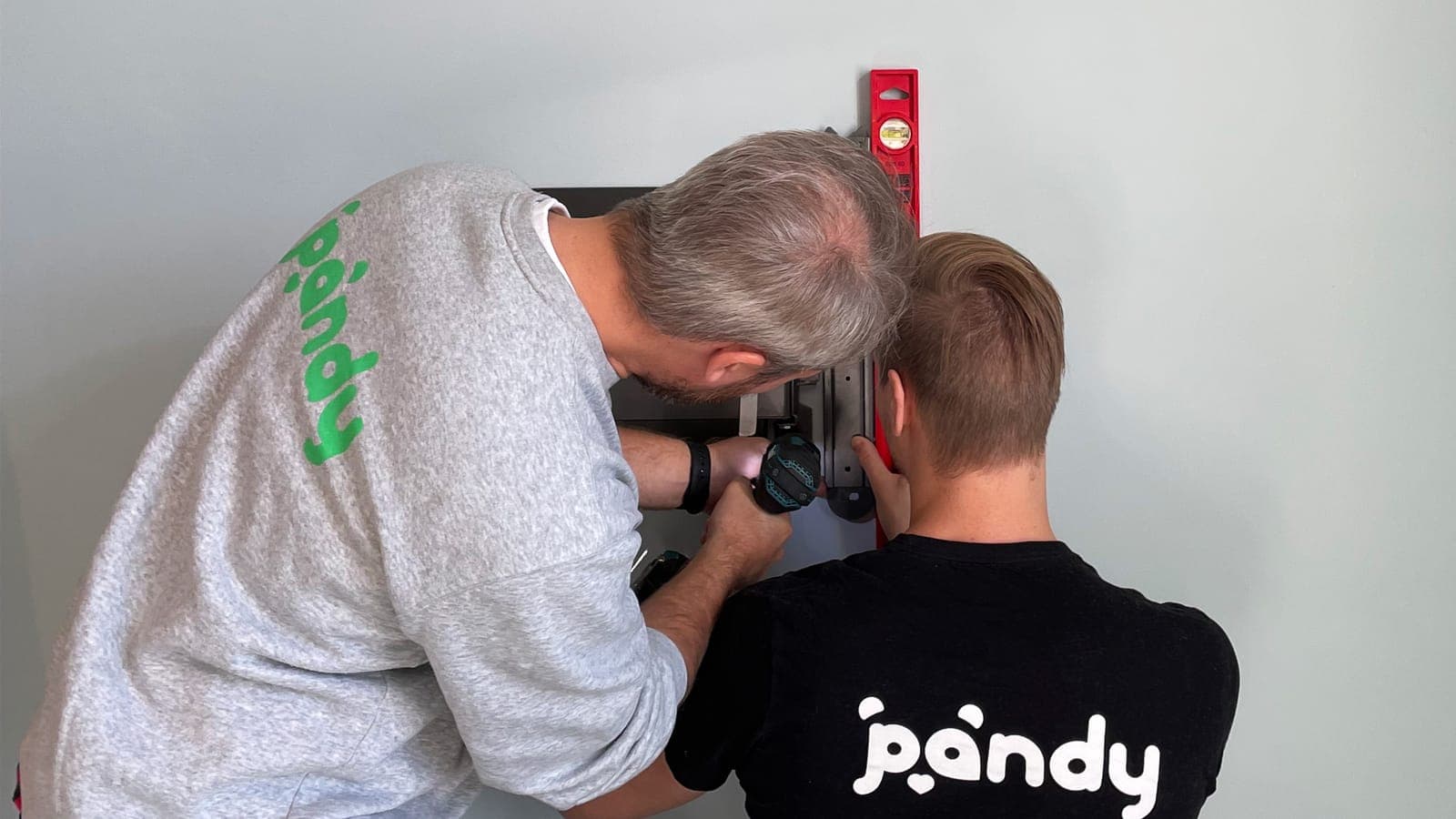 Two Pandy handymen mounting a TV bracket on the wall