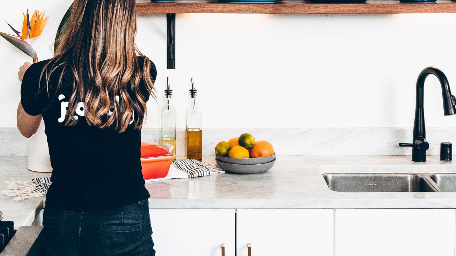 Cleaner with her back to the camera in a freshly cleaned, bright kitchen with a marble countertop
