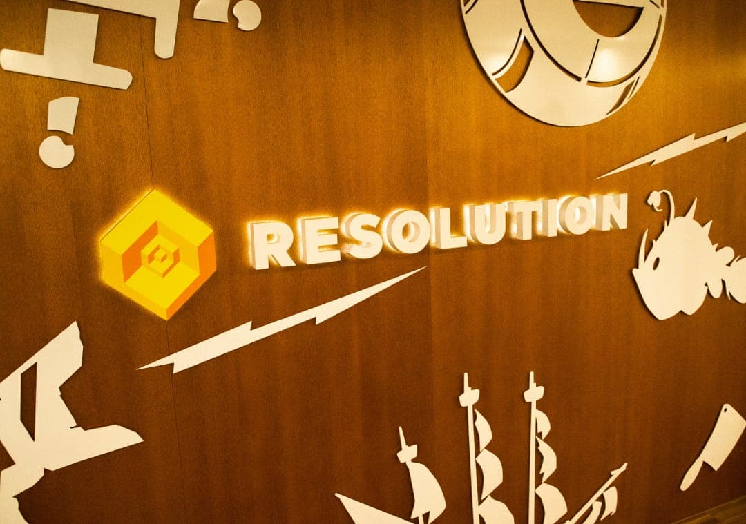 Resolution Games' illuminated logo on a wooden wall in the lobby of their office