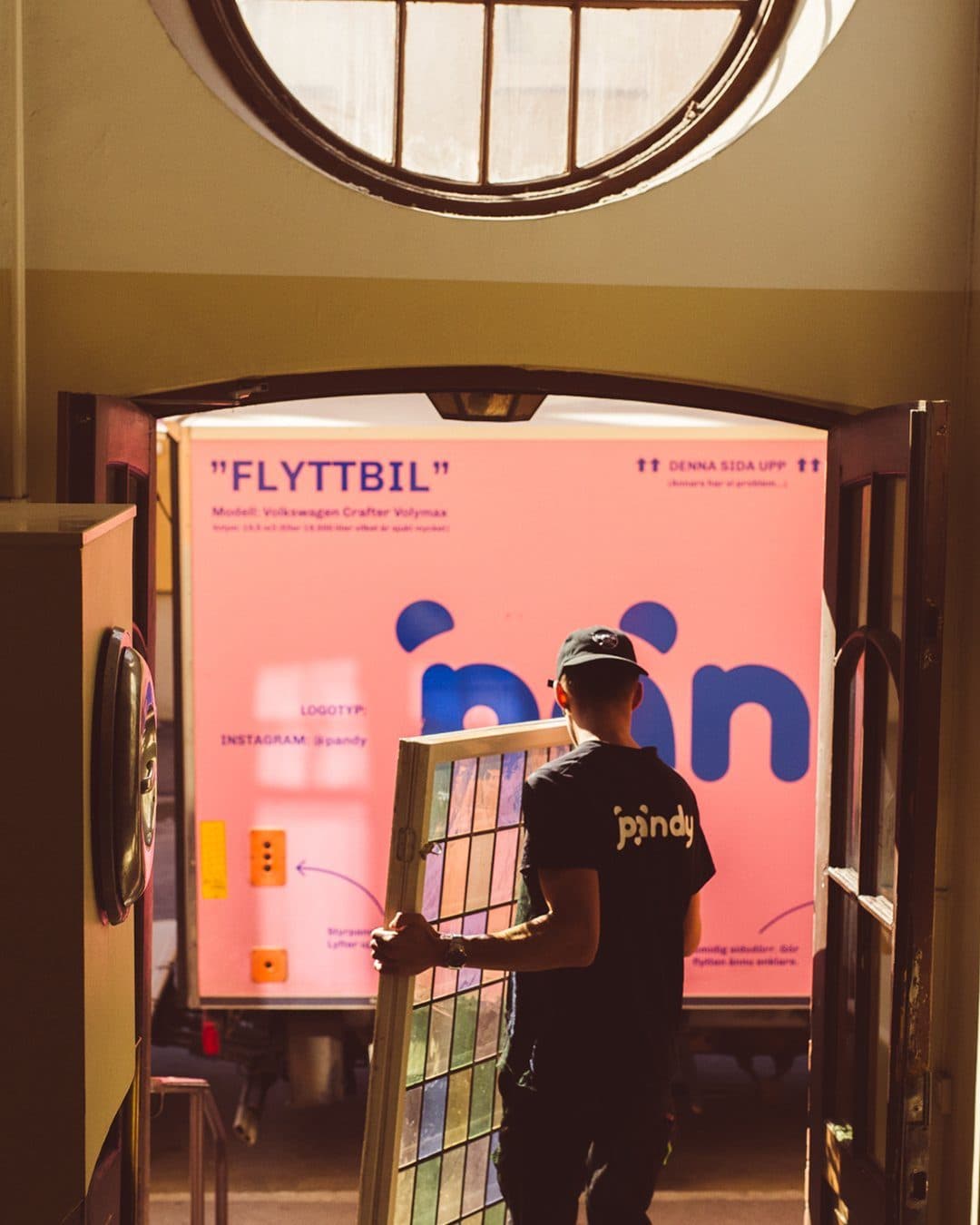 Den rosa Pandy-flyttbilen med texten ”FLYTTBIL” sedd genom en port, en Pandy-medarbetare bär en tavla