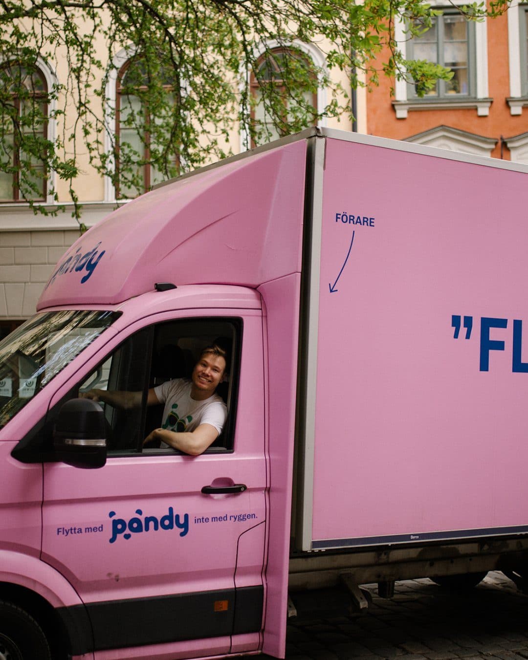 Rosa flyttbil med texten ”FLYTTBIL” och en Pandy-chaufför som vinkar