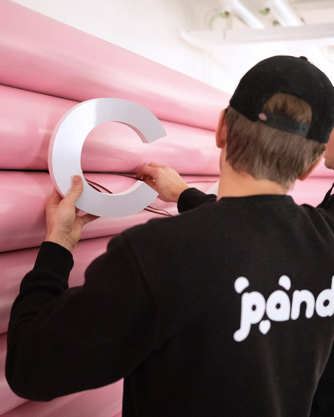 Pandy handyman mounting a large letter on a pink wall