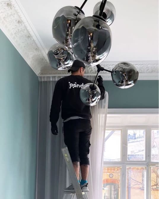 Pandy handyman mounting a curtain rail using a ladder