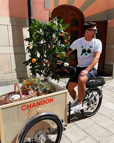 Happy young man in a Pandy t-shirt and sunglasses delivering goods by bike for a business customer